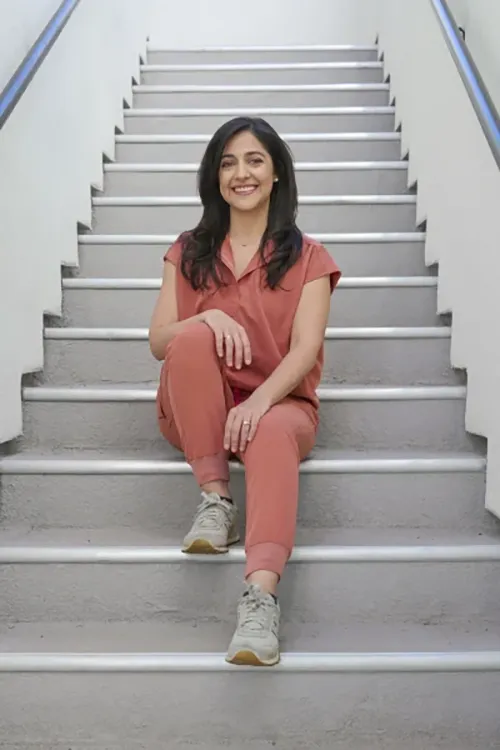 Female physician in coral medical scrubs sitting casually on outdoor concrete stairs smiling warmly